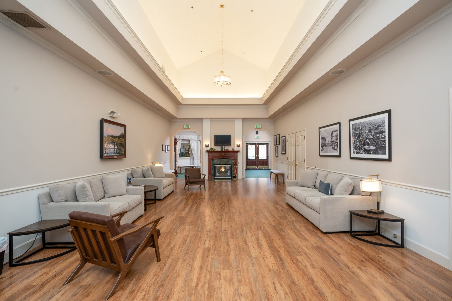 Bright, airy waiting room with gray sofas, wooden chairs, framed art, and a high ceiling.
