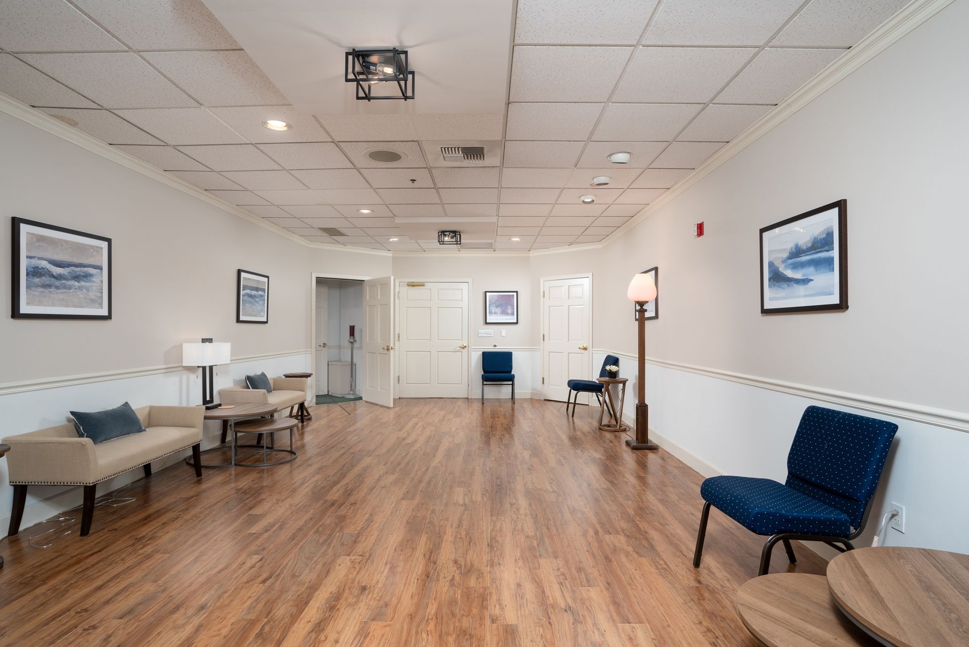 Empty waiting room with wood floors, white walls, blue chairs, and framed pictures