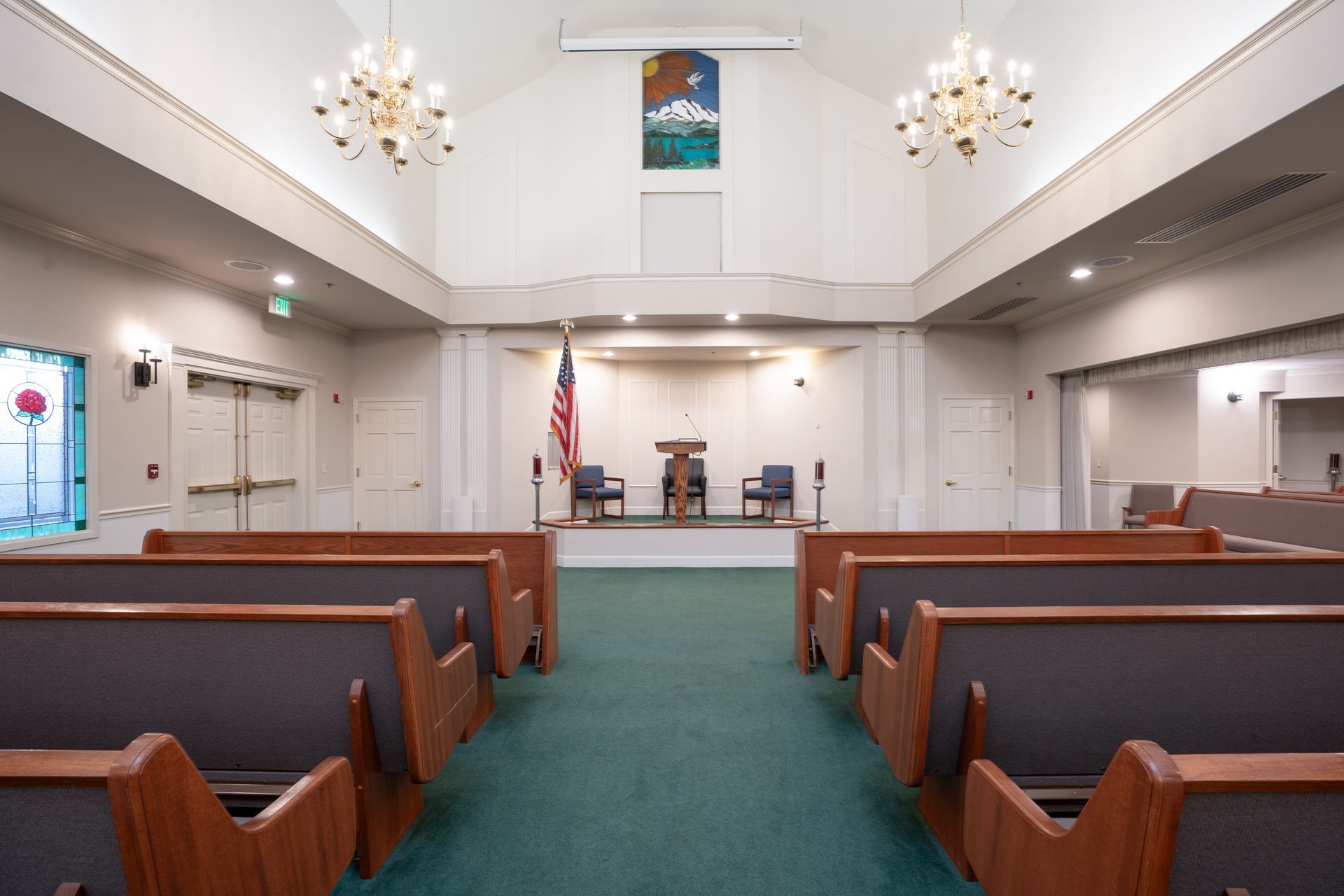 Empty courtroom with wooden benches, green carpet, and a judge’s bench beneath chandeliers