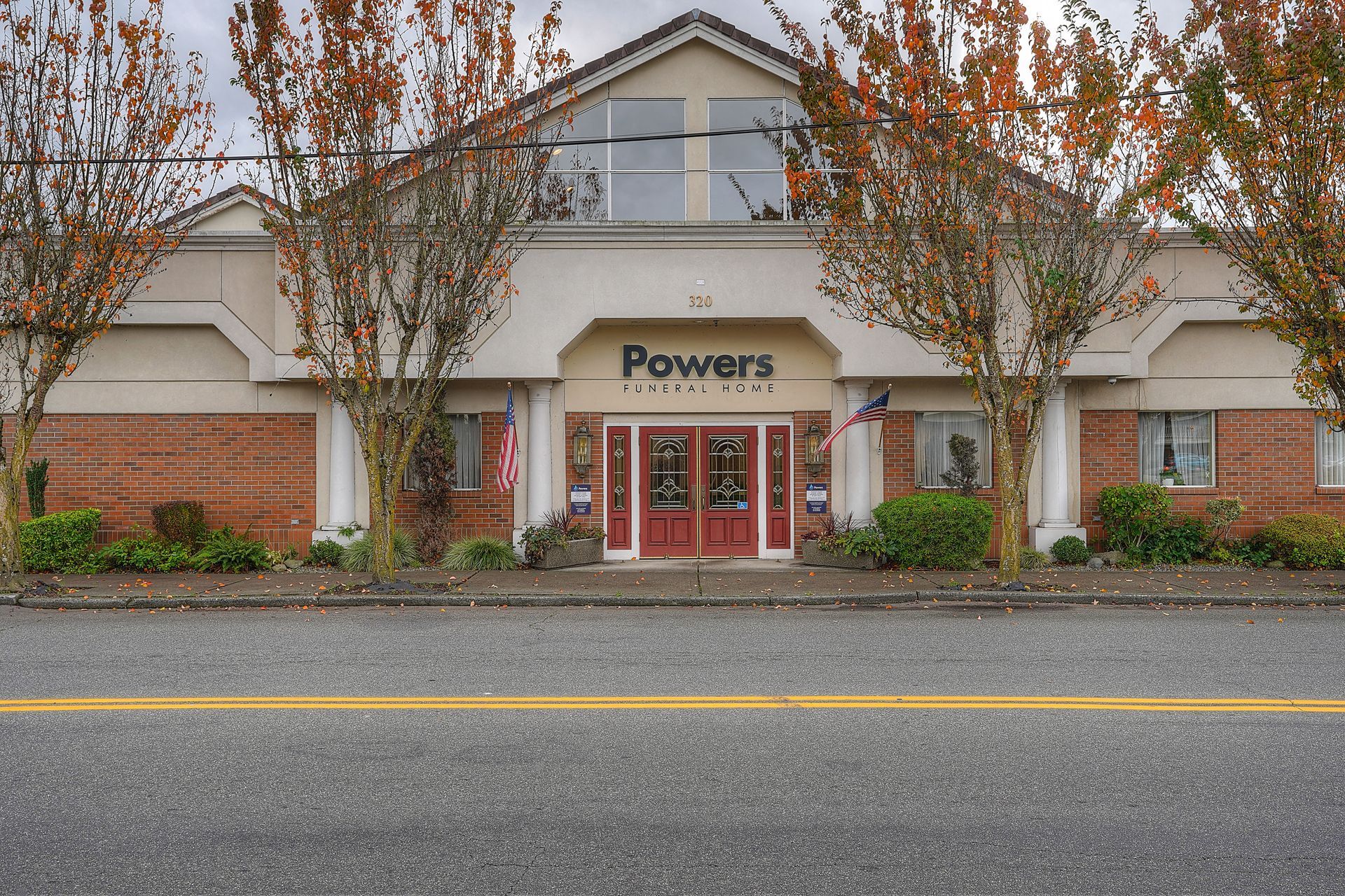 Storefront of Powers with brick facade, red doors, and trees along a parking lot-facing entrance