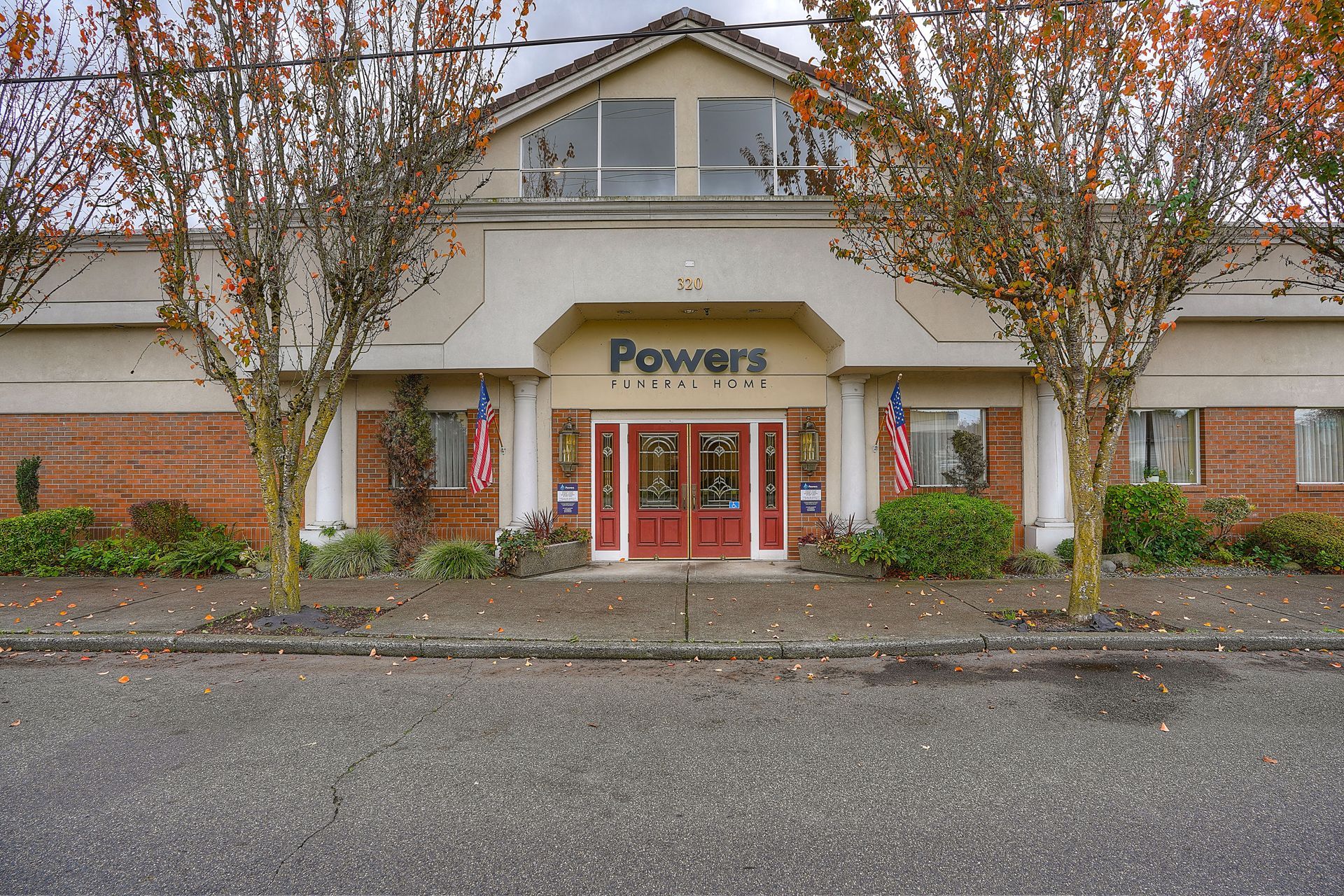 Powers storefront with red double doors, tan siding, and trees lining the front entrance