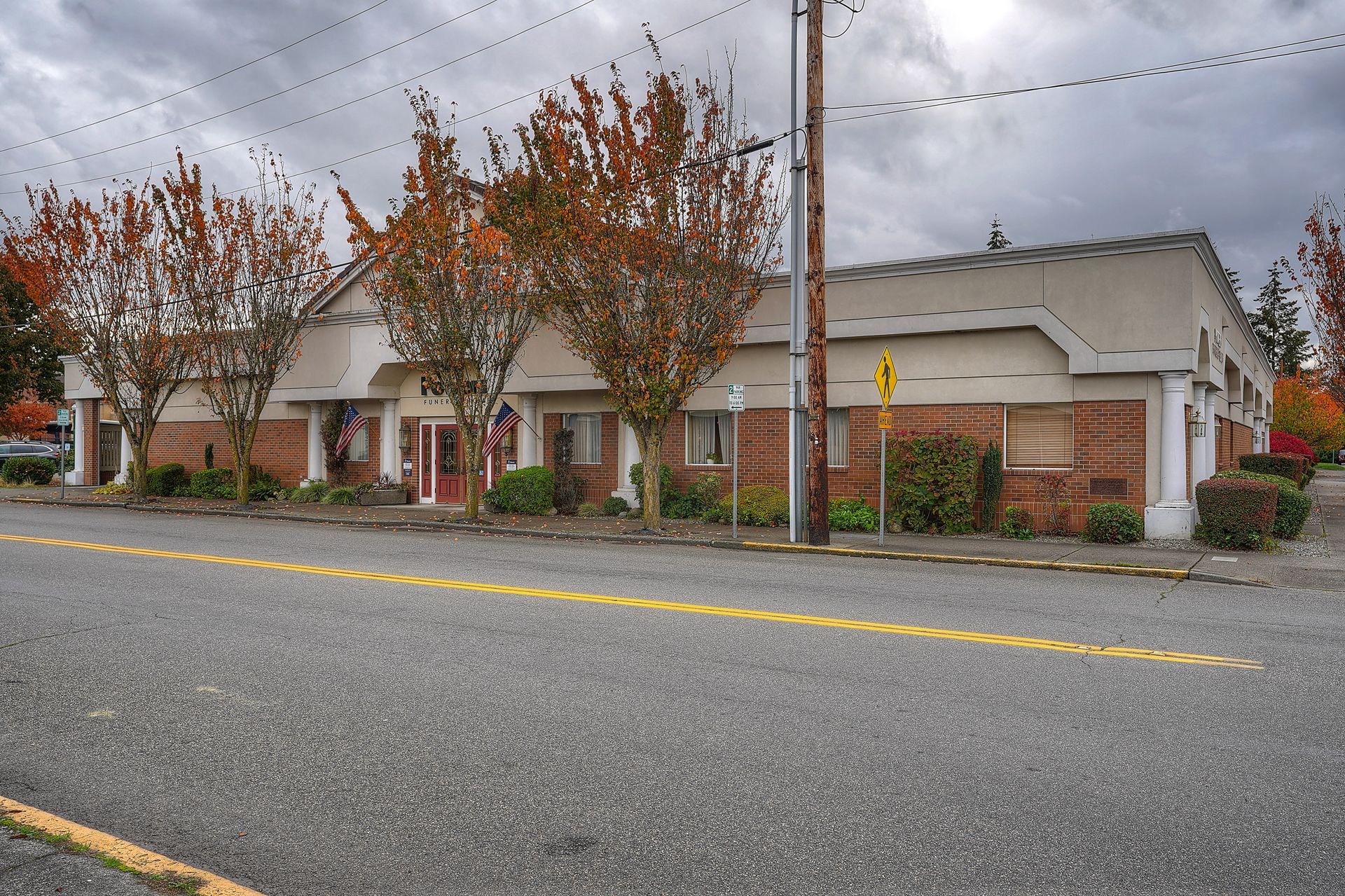 Single-story brick houses along a wet street with trees and a cloudy sky