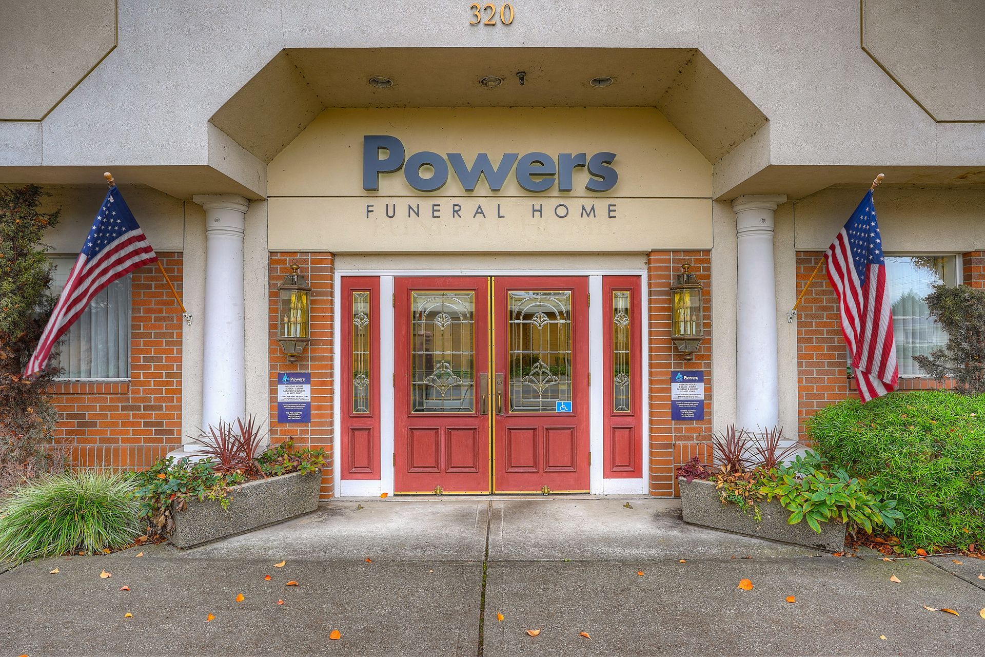 Entrance to Powers Funeral Home with red doors, brick walls, and American flags on both sides.