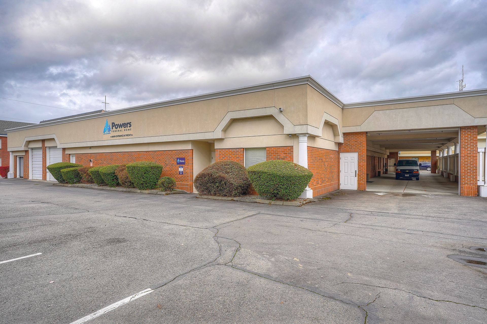 Single-story beige building with brick accents and covered parking under a cloudy sky
