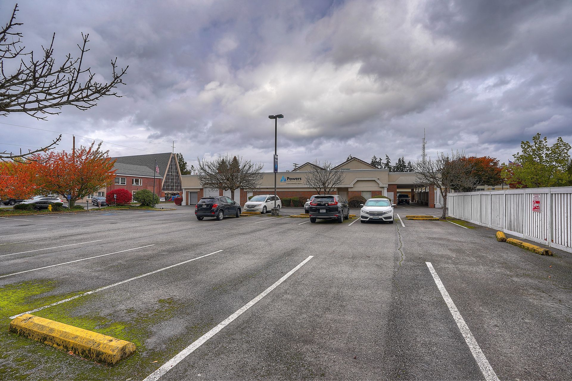 Empty gravel parking lot with a few parked cars under cloudy skies
