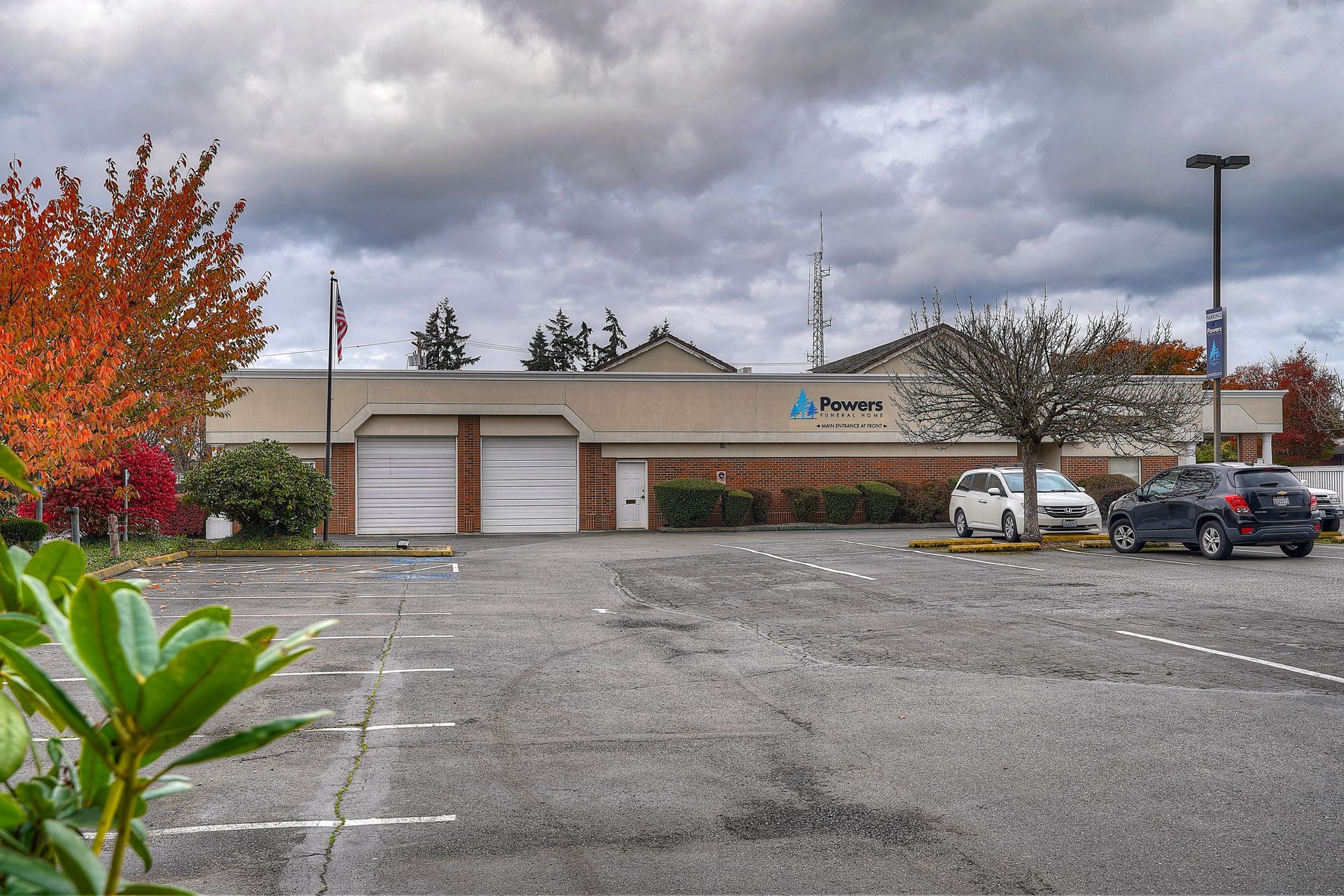 Parking lot in front of a low commercial building under cloudy skies, with cars parked on the right.