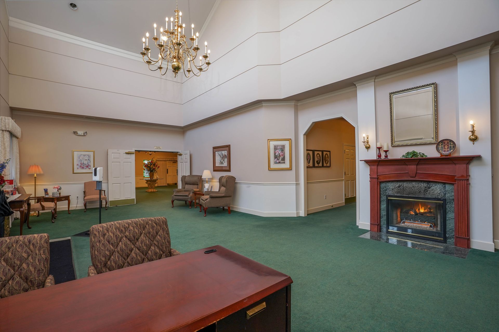 Spacious lounge with green carpet, chandelier, and fireplace in a historic room