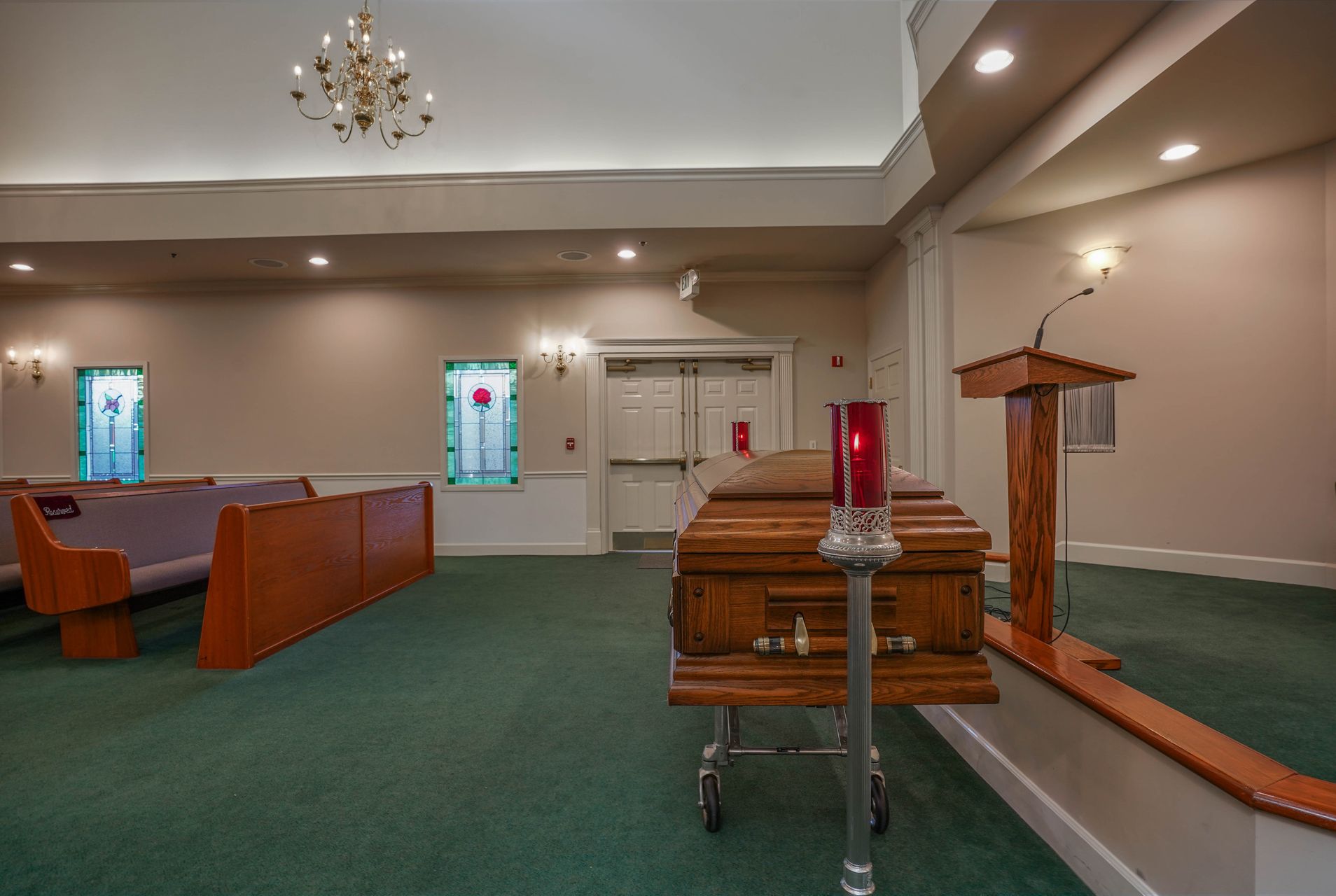Church sanctuary with green carpet, wooden pews, pulpit, and stained-glass windows