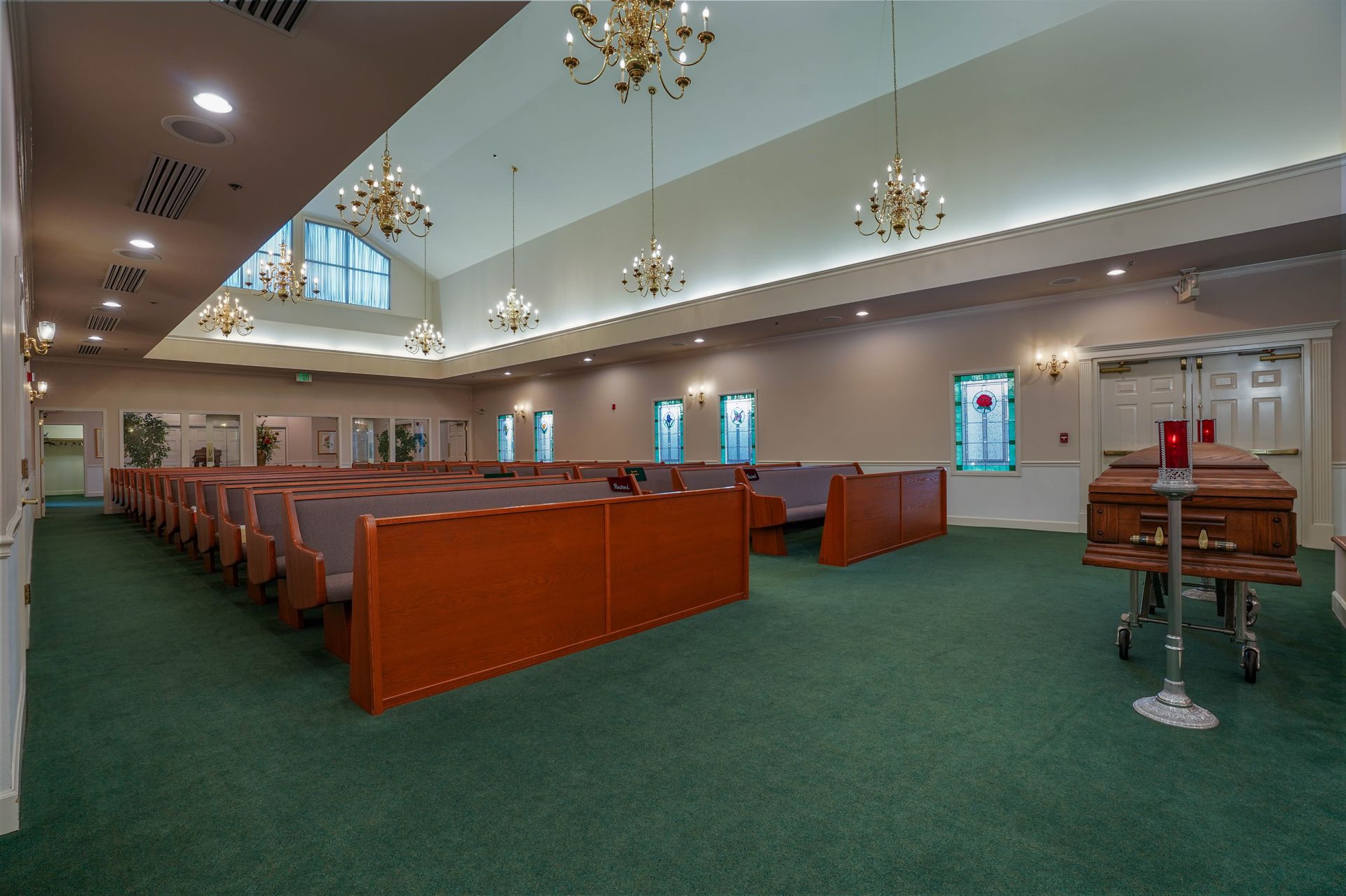 Empty church sanctuary with green carpet, wooden pews, and chandeliers hanging from the ceiling
