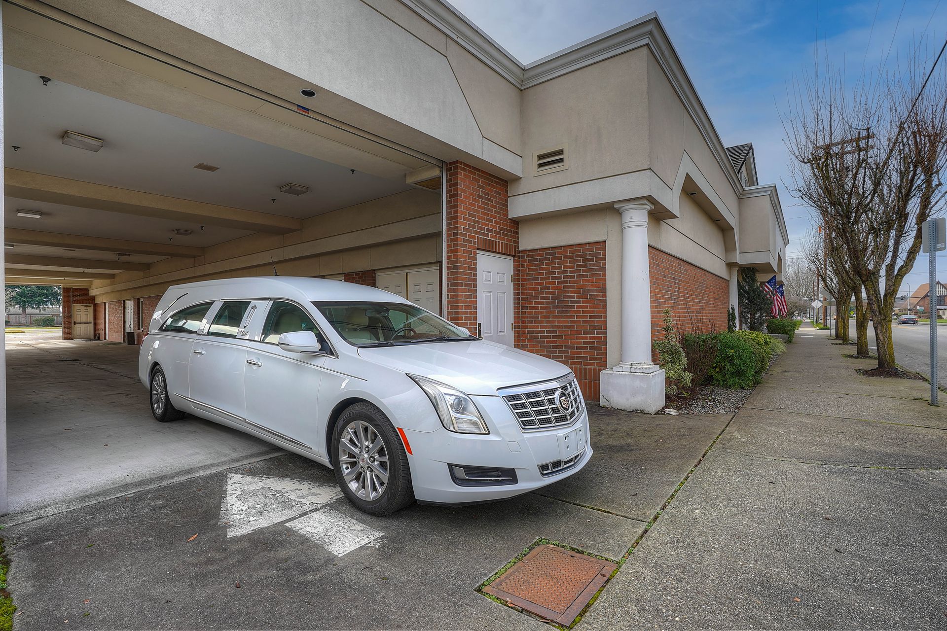 Silver sedan parked under a covered building entrance with brick columns and a sidewalk nearby