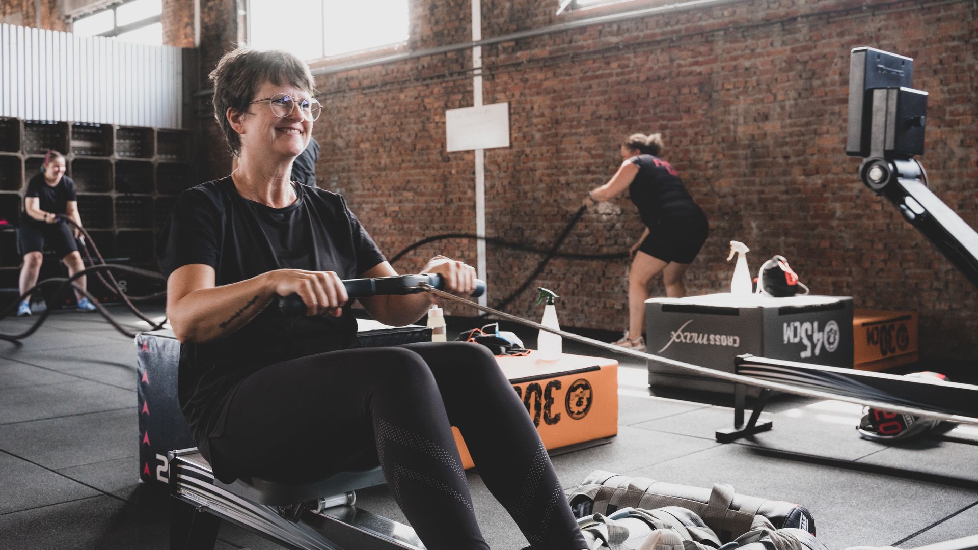 Een indoor roeitraining in een sportschool met bakstenen muren, waarbij atleten tijdens hun training op roeimachines roeien.