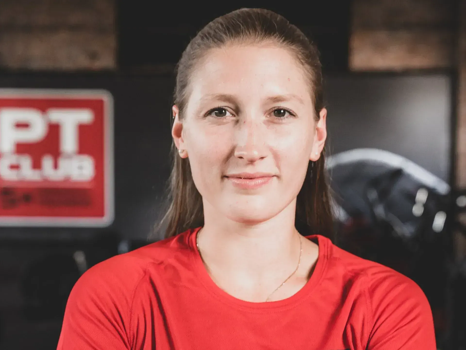 Vrouw in een rood shirt kijkt in de camera in een sportschool.