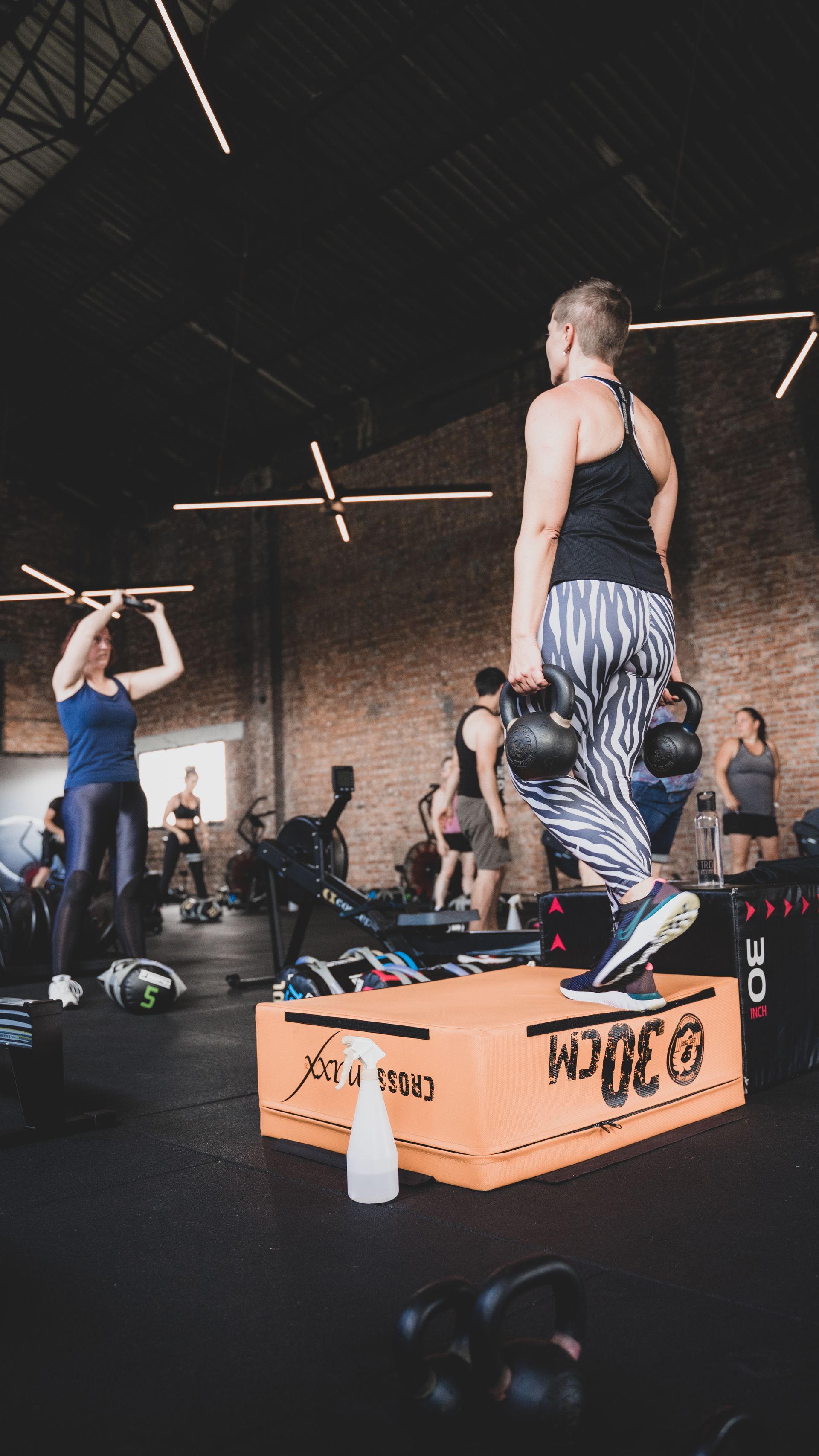 Mensen die aan het sporten zijn in een sportschool, met een vrouw die op de voorgrond balanceert op een oranje doos.