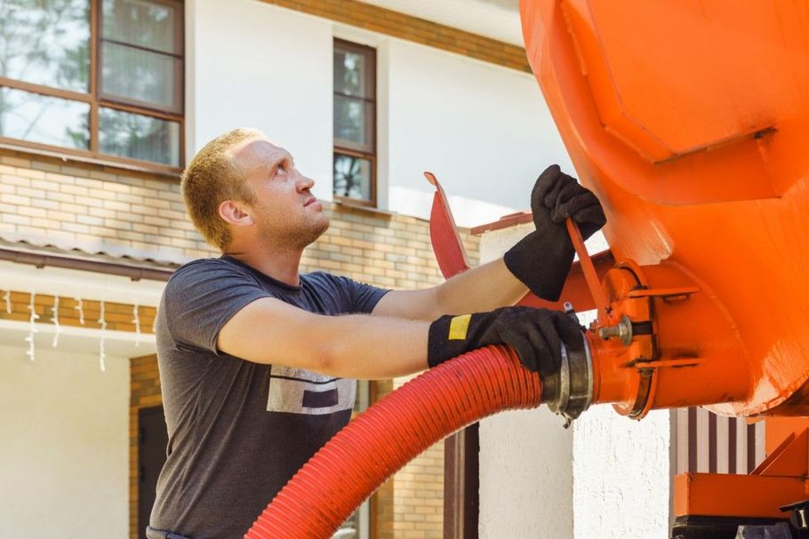 Worker connecting a red hose to an orange truck at a house driveway