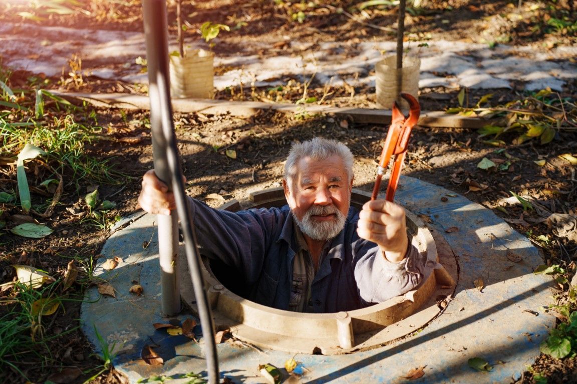 Man climbing out of a manhole, holding a rope in a sunlit outdoor area