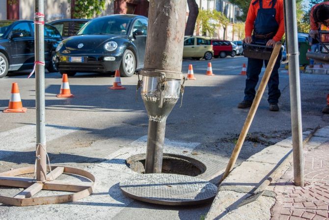 Roadwork crew repairing a sidewalk hole with cones, tools, and a worker nearby in the street