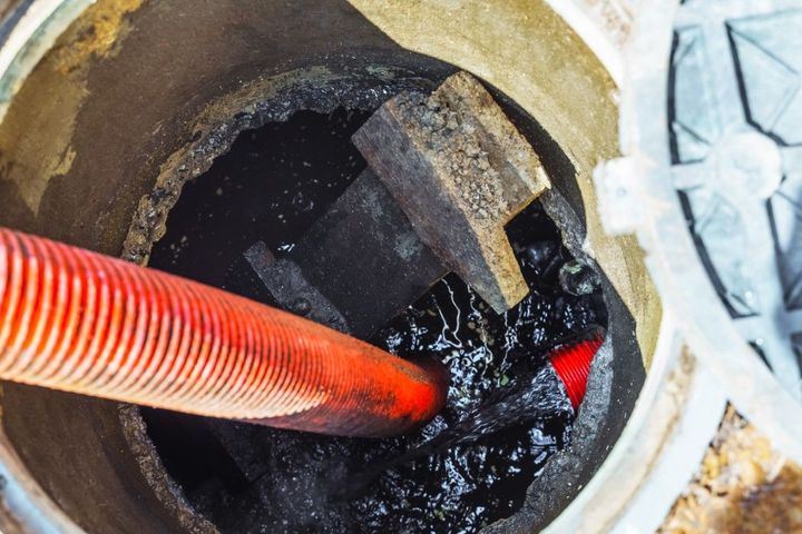 Orange hose draining water from a dark manhole or sewer opening