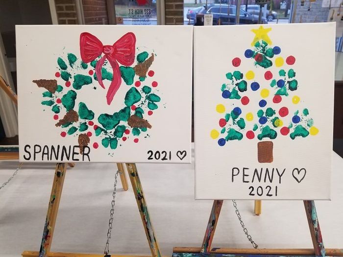 Two holiday art boards on easels: wreath labeled “Spanner 2021” and Christmas tree labeled “Penny 2021”