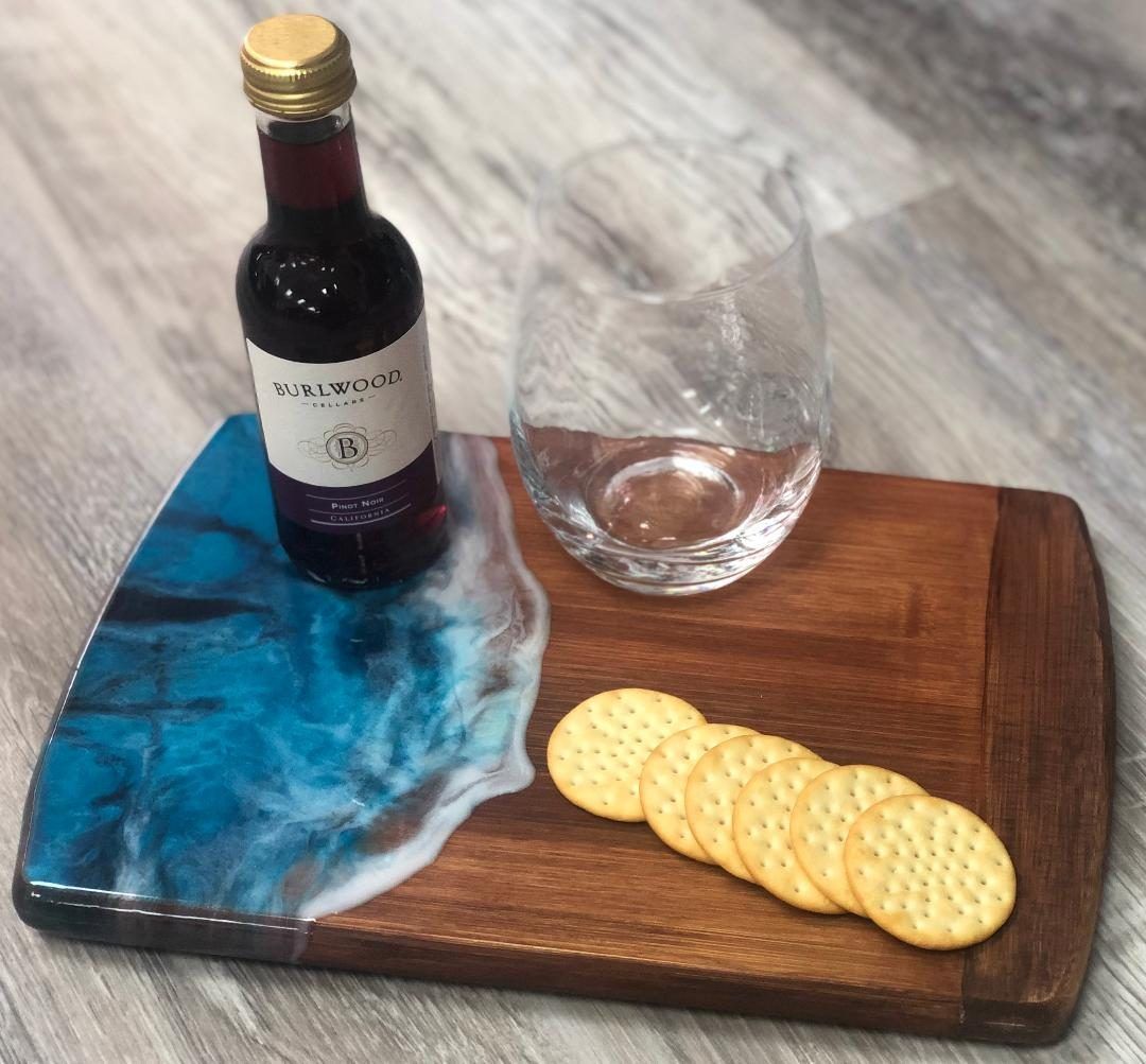Bottle of red wine, empty glass, and crackers on a wooden serving board with blue resin detail