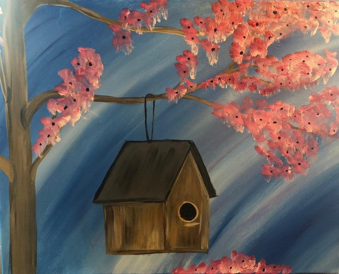 Wooden birdhouse hangs before blue sky and pink cherry blossoms