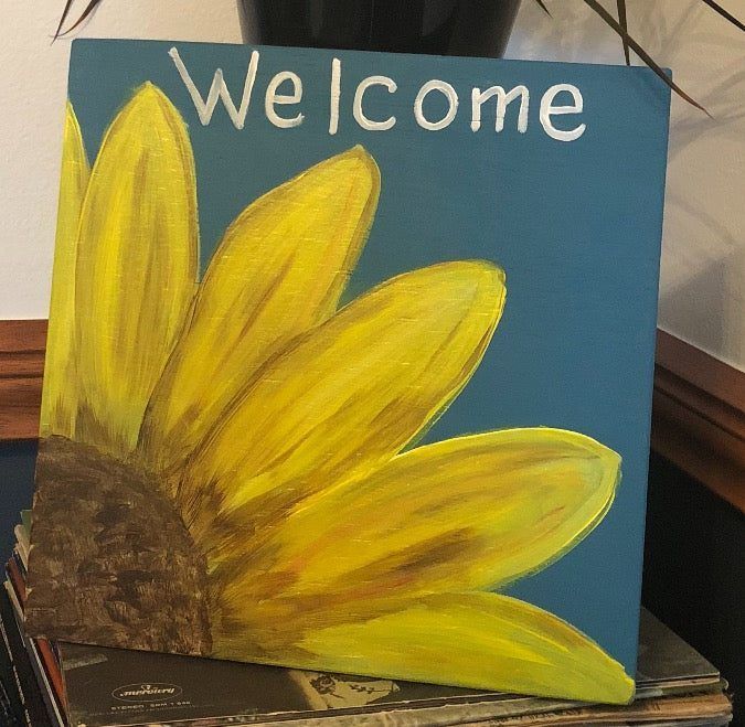 Hand-painted welcome sign with a large yellow sunflower on a blue background