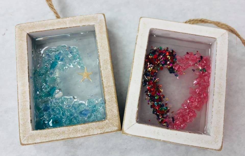 Two small framed resin art pieces: blue starfish on the left, pink heart with glitter on the right.