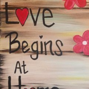 Handwritten “Love Begins At” with a red heart and pink flowers on a wood-look background