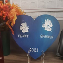 Blue heart plaque with white paw prints labeled “PENNY” and “SPANNER,” with “2021” at the bottom.