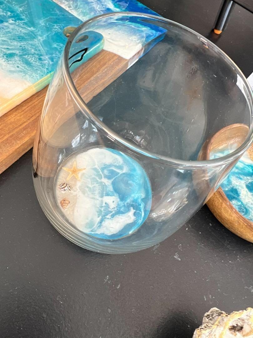 Clear glass tumbler with a blue-and-white sphere inside, on a dark tabletop near a wooden tray.