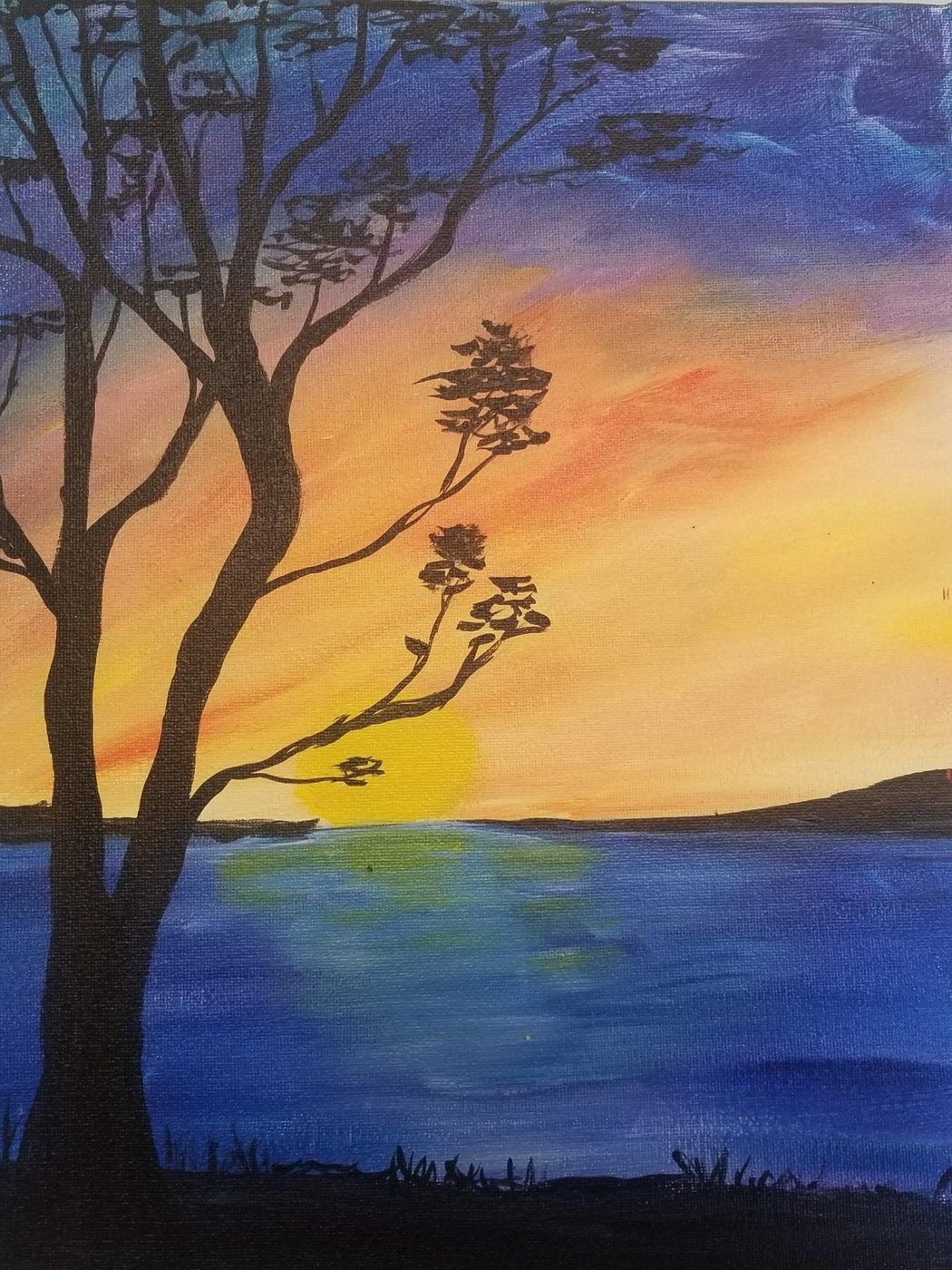 Silhouette of a tree by a blue lake at sunset, with a yellow-orange and purple sky.