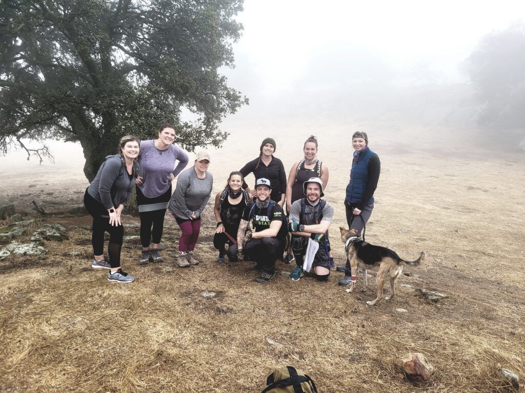 Group of hikers posing with a dog in a foggy field near a tree
