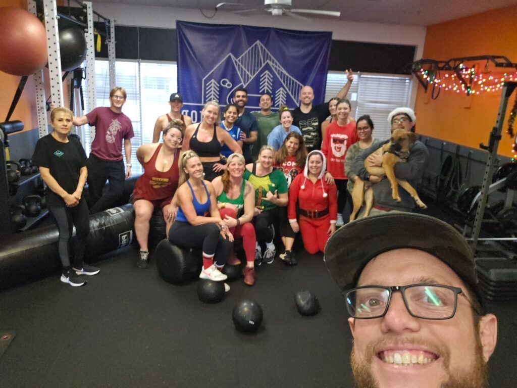 Group of people posing in a gym, smiling with kettlebells in front of a purple banner.