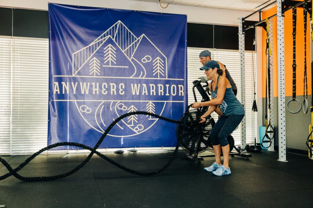 Person exercising with battle ropes in a gym beside an “Anywhere Warrior” banner