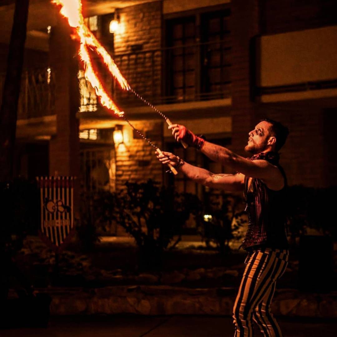 Fire performer swinging a flaming staff at night in a dimly lit courtyard