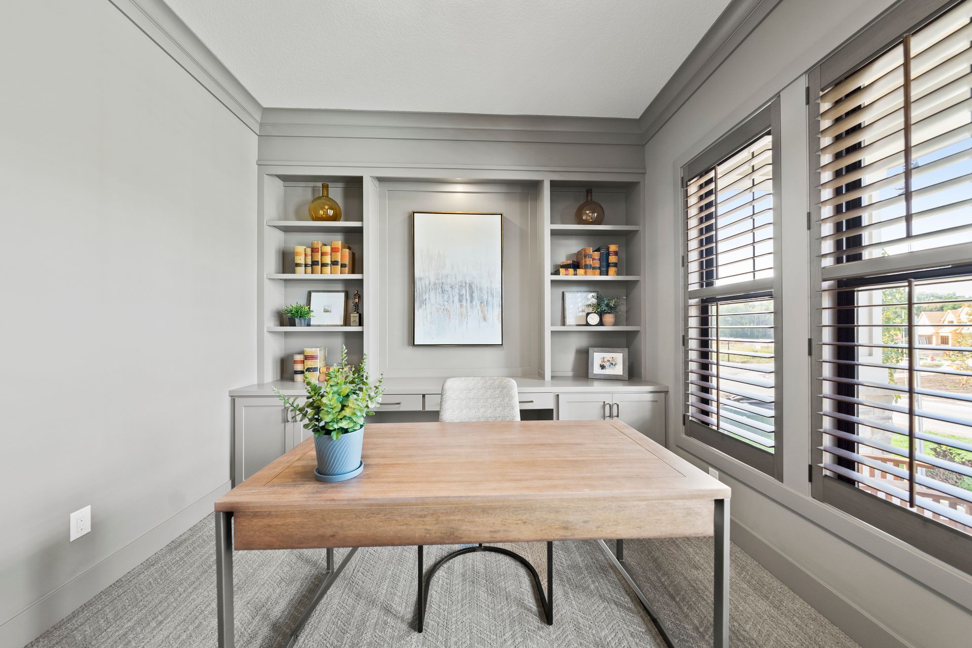 A home office with a desk , chairs , shelves and shutters.