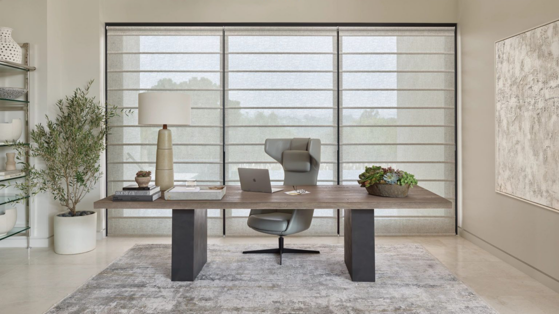 Modern home office with a desk, chair, and art, neutral colors. Hunter Douglas Alustra® Woven Textures® shades on floor to ceiling windows.