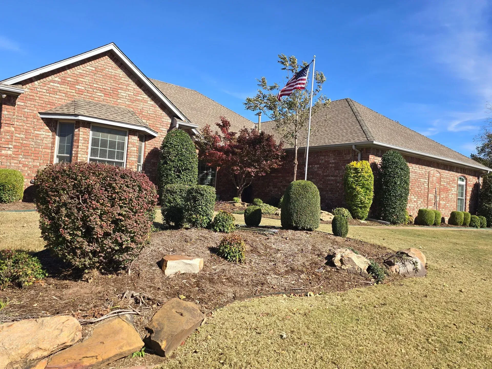 Brick house with manicured shrubs and an American flag in a sunny front yard