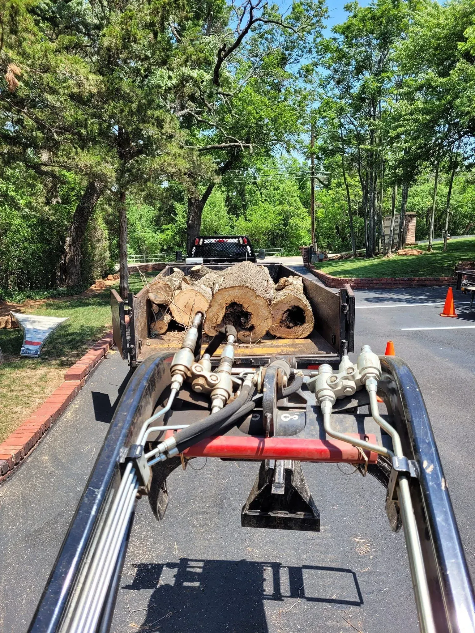 Road work truck hauling a mud-covered vehicle frame on a tree-lined street
