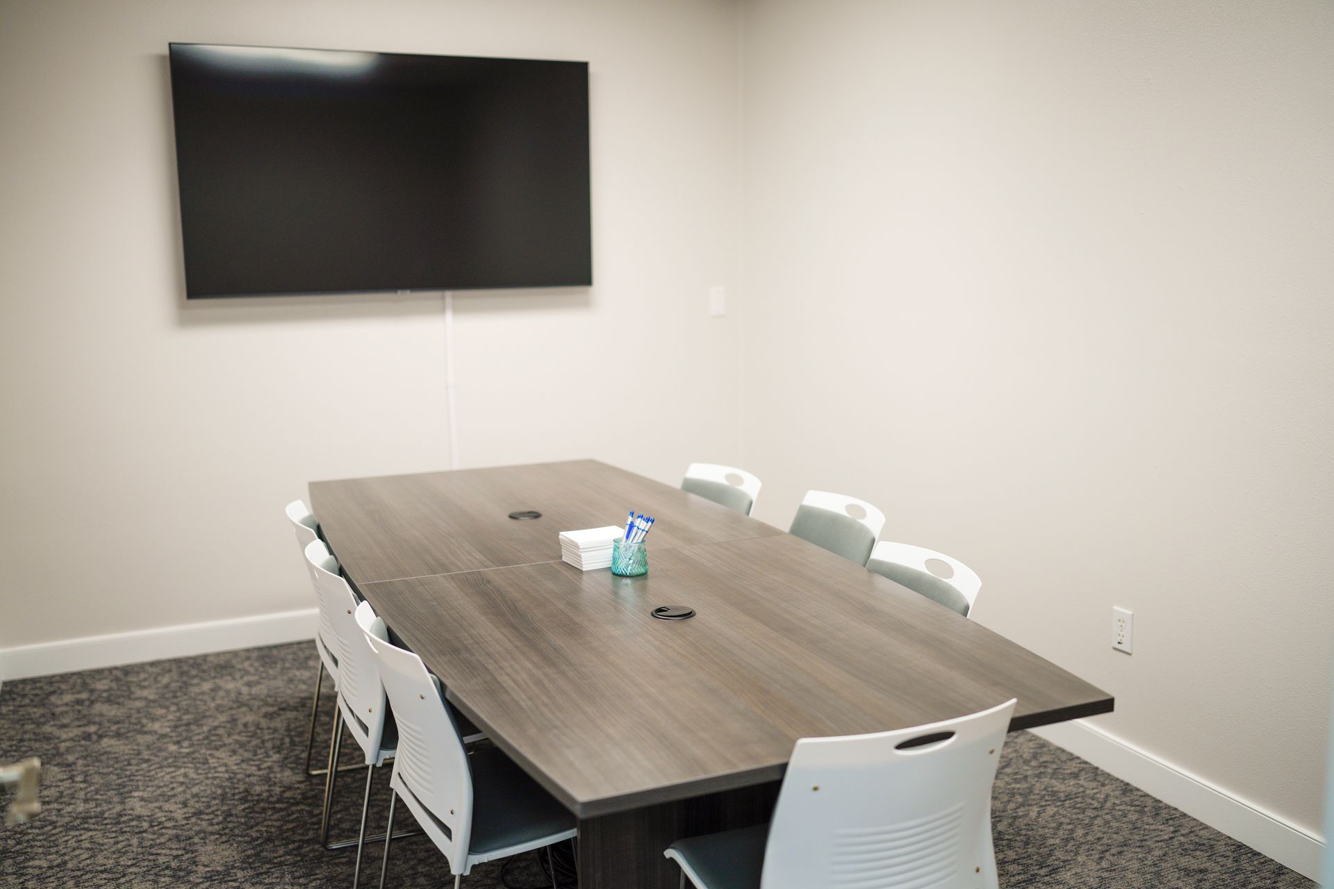 A conference room with a long table and chairs and a flat screen tv on the wall.