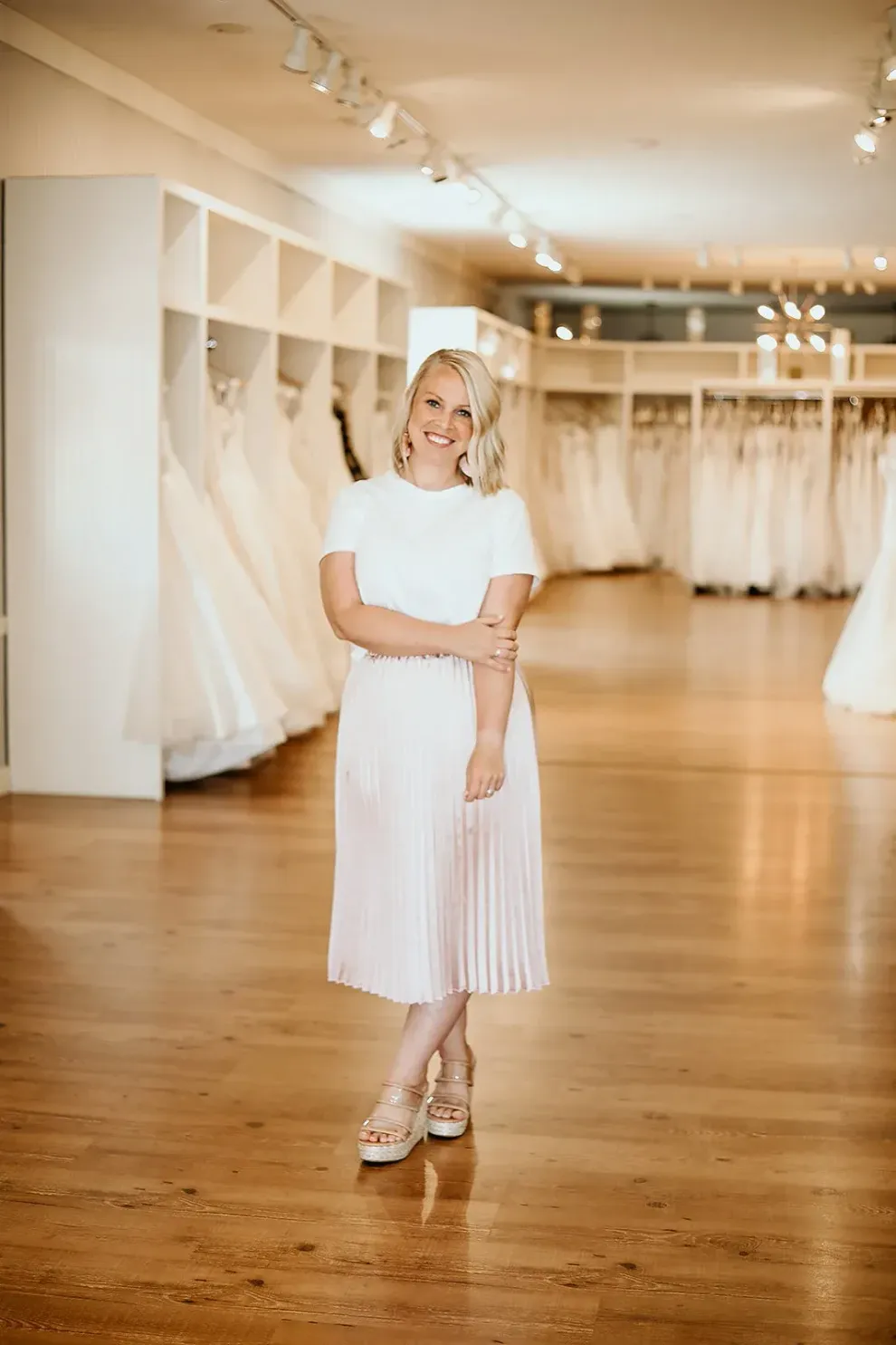 Blonde woman in white dress stands in wedding dress boutique.