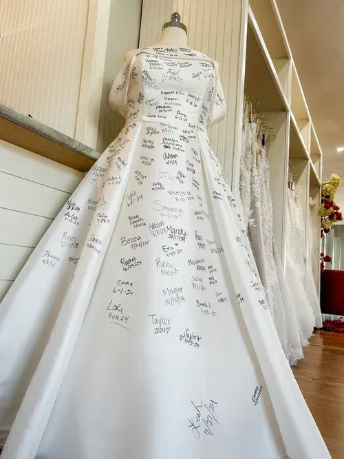 A white wedding dress covered in signatures, on a mannequin in a bridal shop.