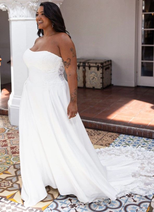 Woman in a white strapless gown standing on a porch with a long train, smiling to the side.