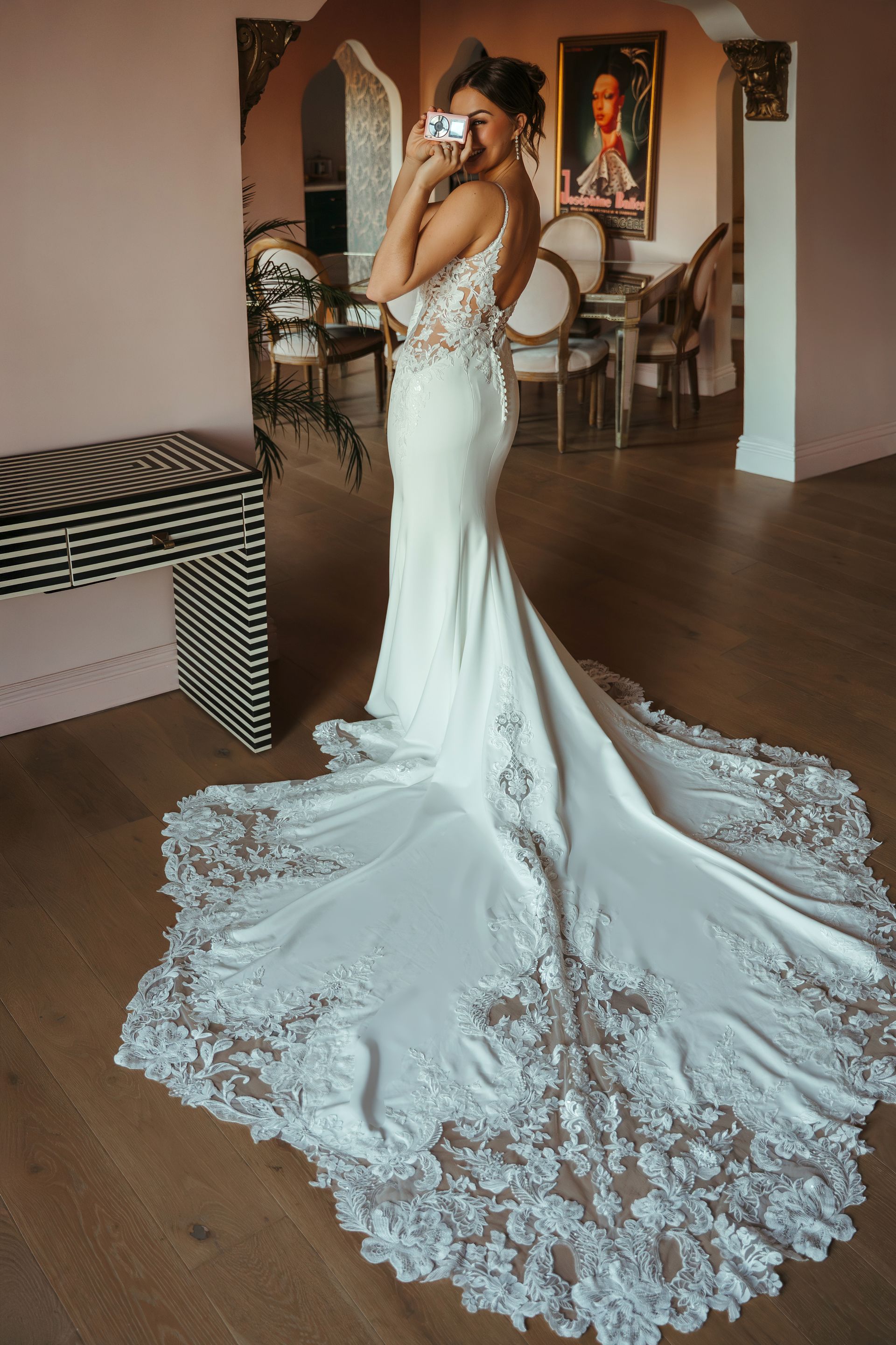 Person in a white lace wedding gown with long train, posing indoors in a living room