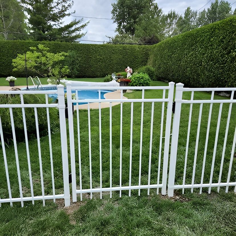 White fence surrounds a grassy yard with a swimming pool in the background, surrounded by hedges and trees.