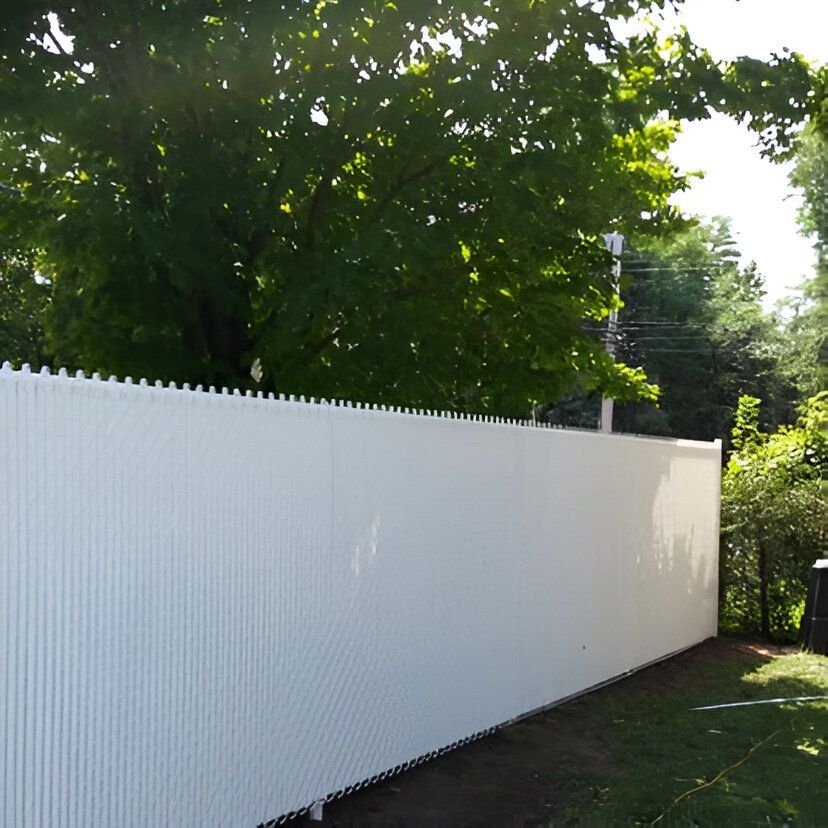 White privacy fence in a yard, with green trees overhead and sunlight.
