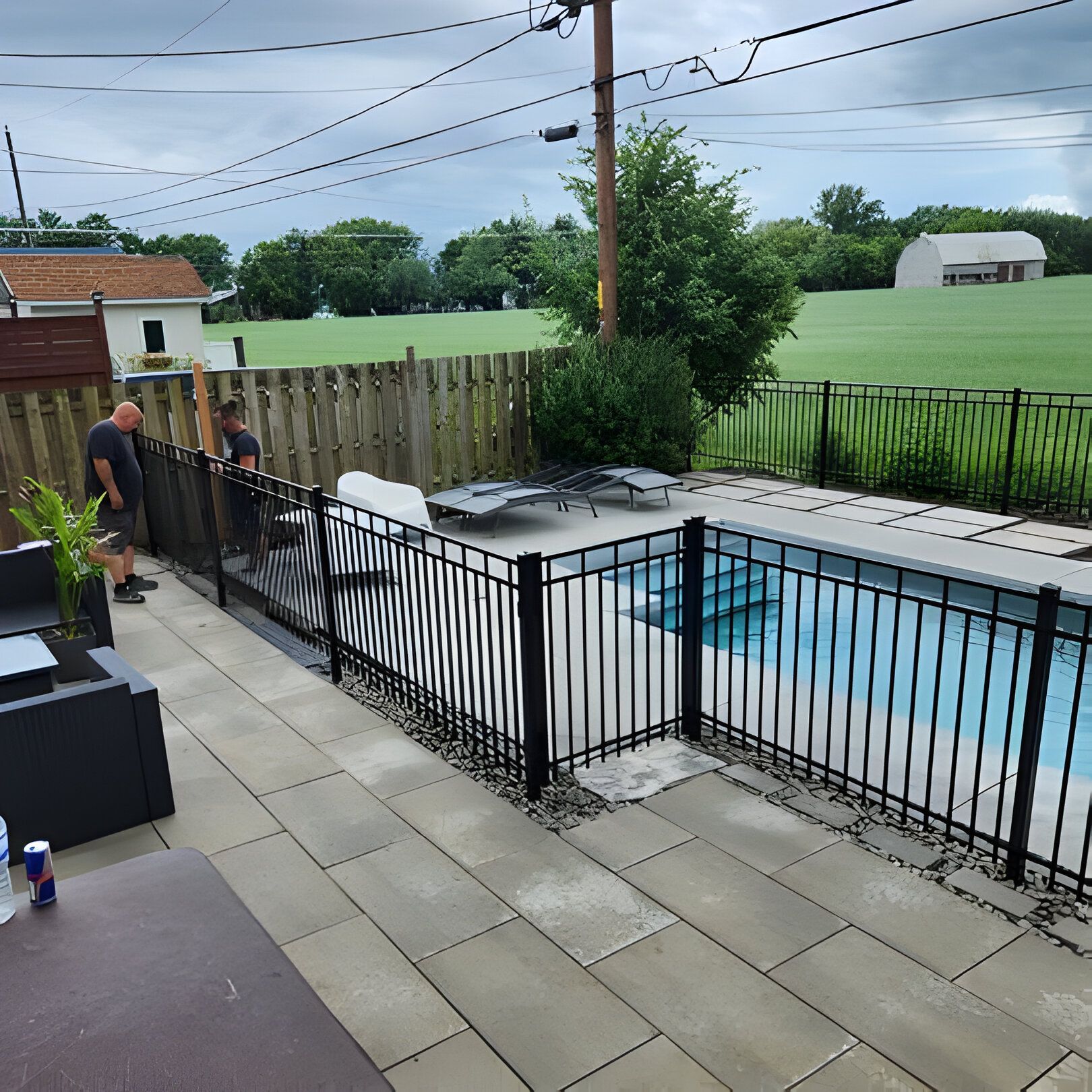 Black fenced-in pool in a yard with a patio. Two men stand near the fence.