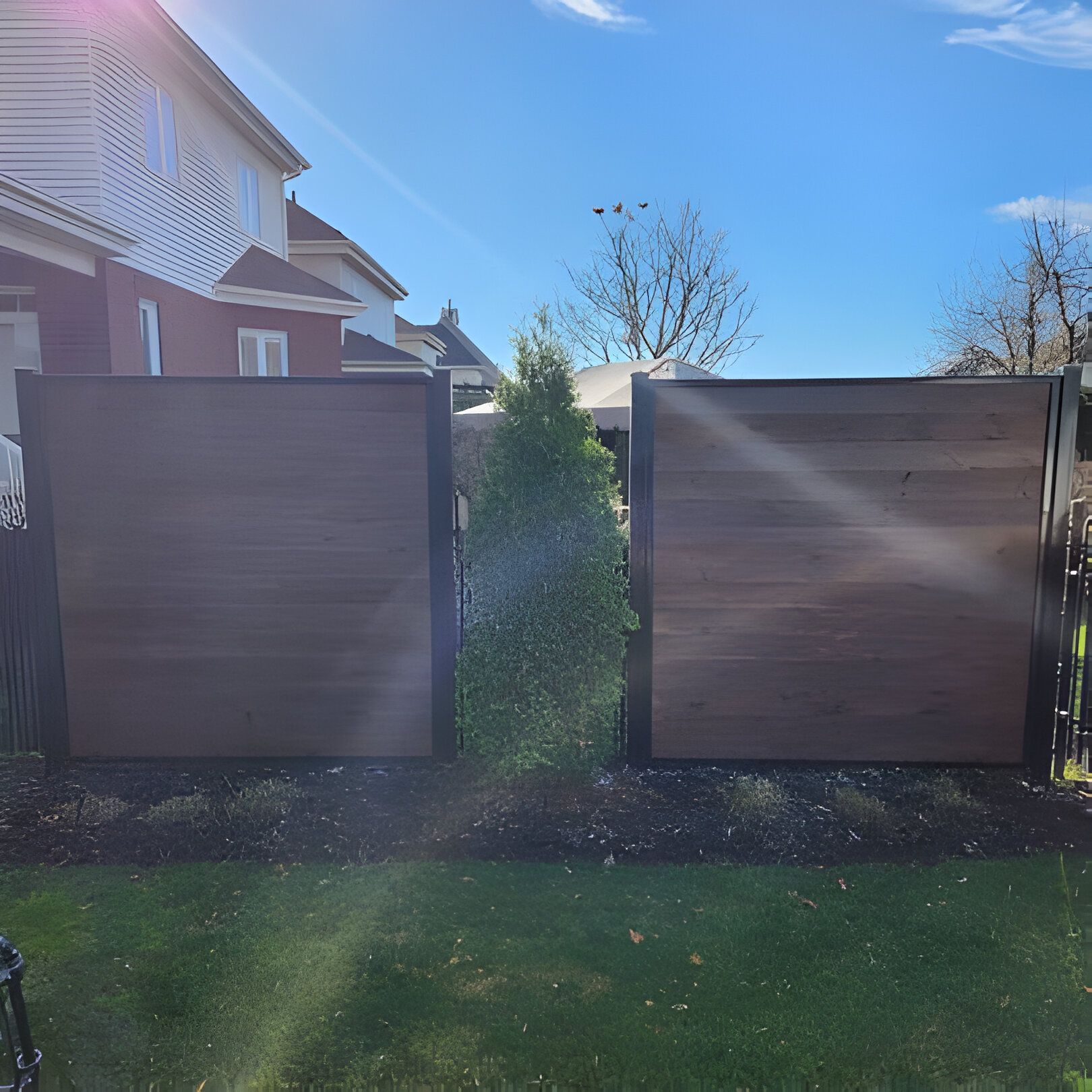 Brown wooden fence panels with a gap, green grass, and a blue sky.