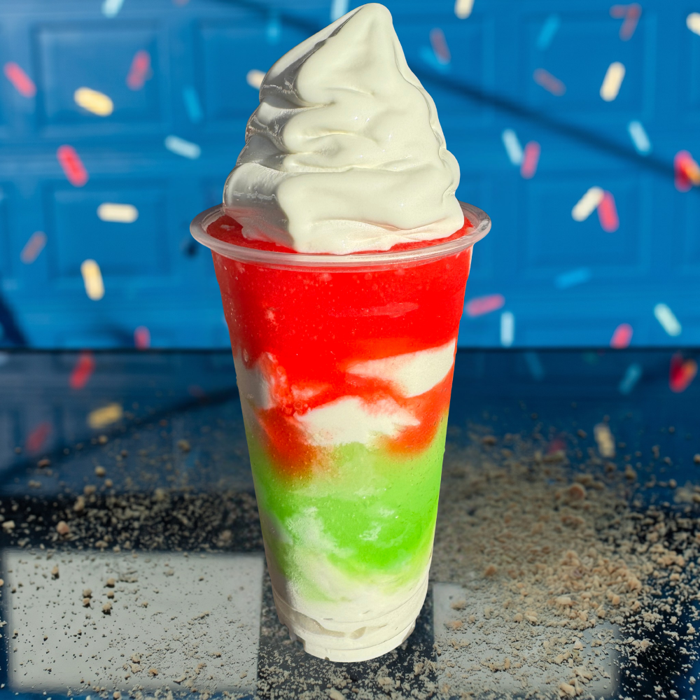 Colorful red, green, and white soft-serve dessert in a clear cup against a blue background