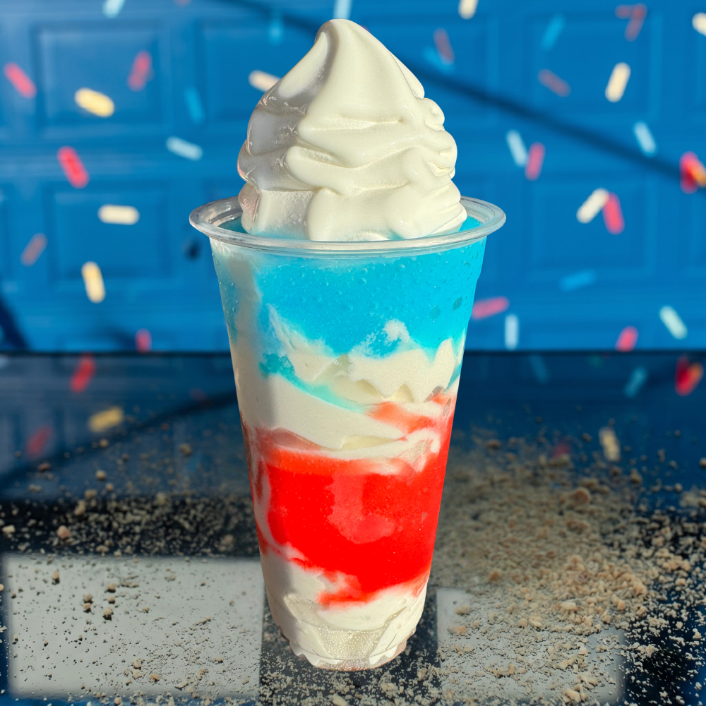 Clear cup of vanilla soft serve layered with red and blue syrup, against a blue backdrop with sprinkles