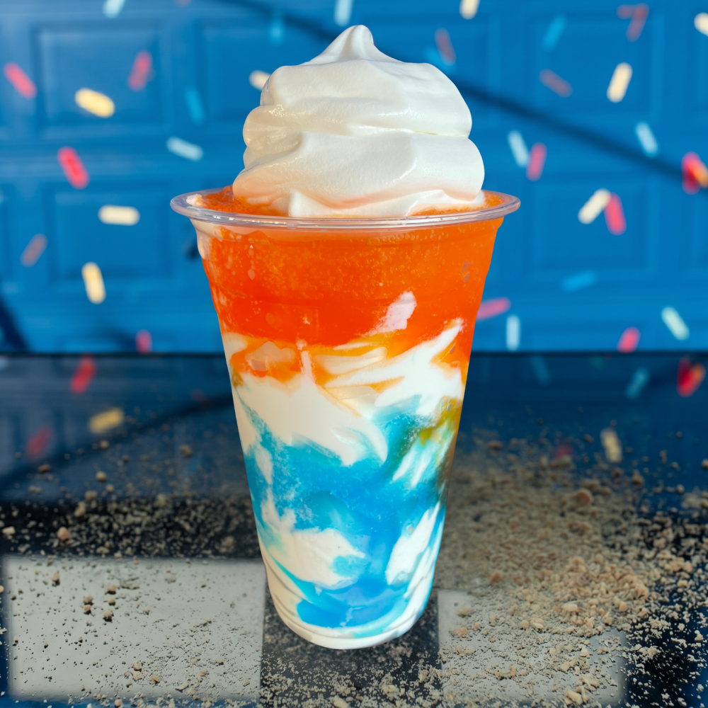 Swirled orange, blue, and white frozen dessert in a clear cup against a blue background